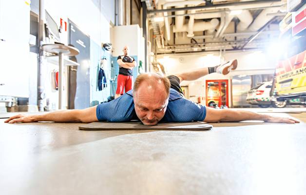 Palomies Reiska Taipale tekee paloaseman kalustohallissa lantion liikkuvuutta parantavaa venytystä. Antti Juselius tarkkailee harjoitusta.