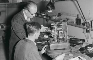 Oppipoika saa opastusta vanhemmalta työntekijältä. Osuustukkukaupan korjaamolla Helsingissä asetettiin kassakoneen kuitti- ja värinauhamekanismia paikoilleen vuonna 1955.